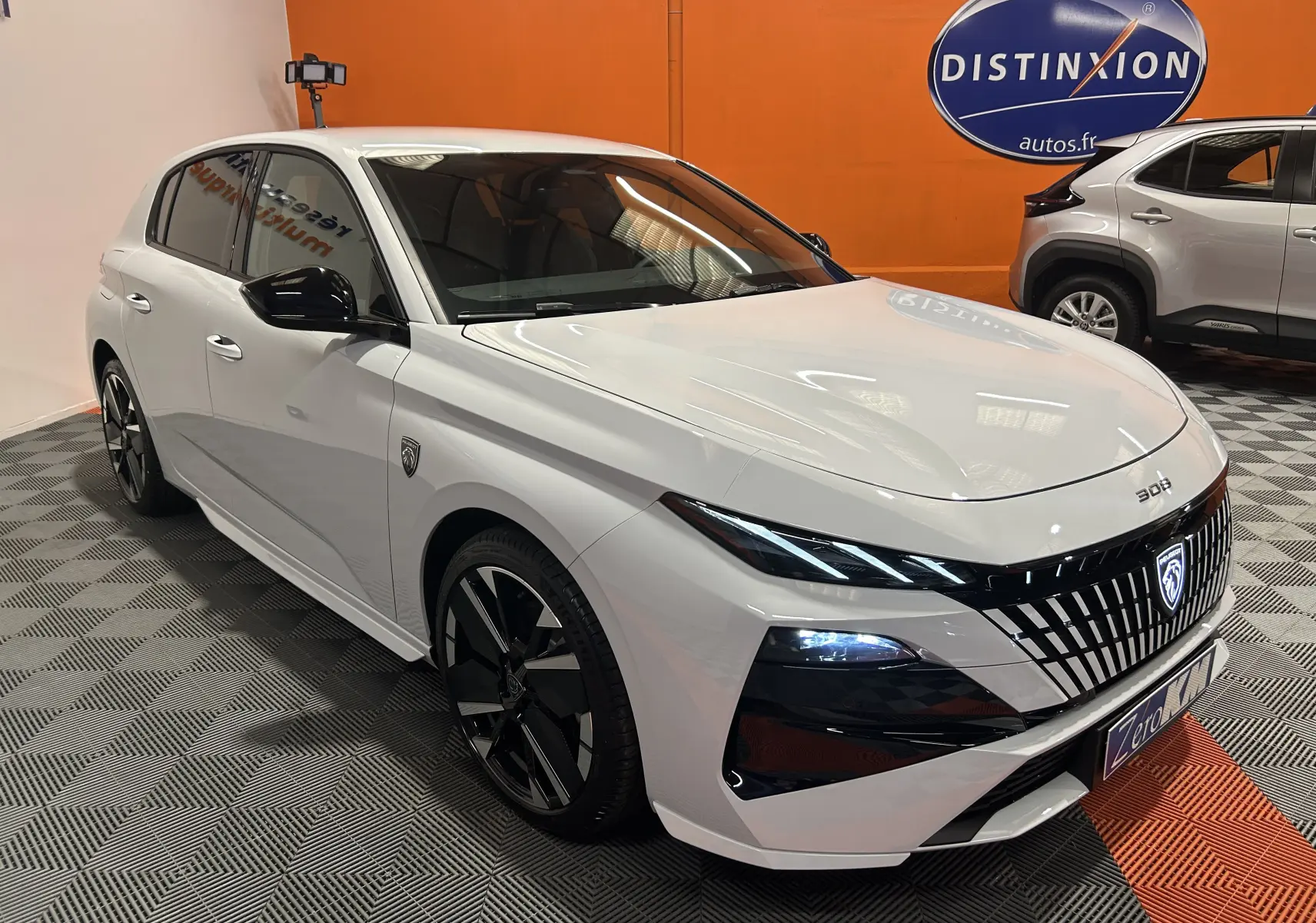Peugeot 308 III Ph.2 Hybrid blanc Okenite vue 3/4 avant droit avec calandre verticale et jantes noires.
