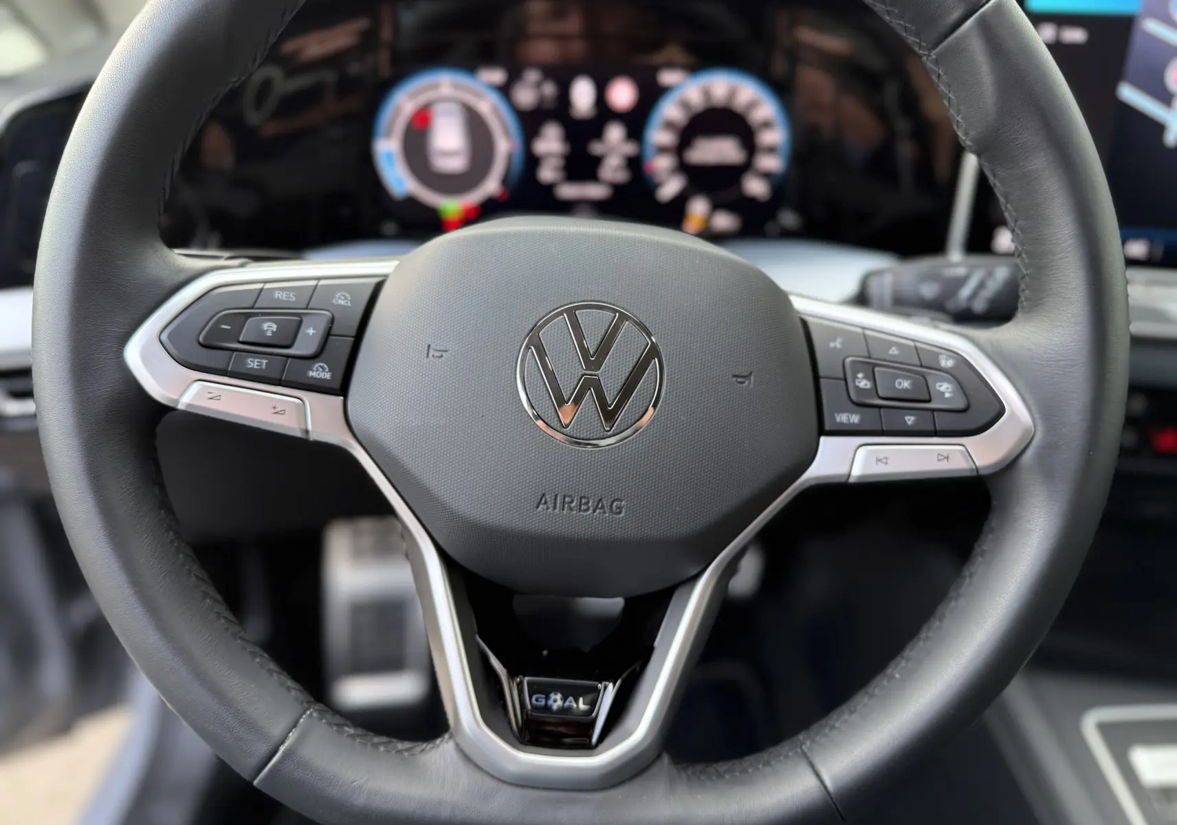 Gros plan sur le volant cuir noir du Volkswagen Golf SW 2.0 TDI 150 GOAL avec commandes intégrées et logo central visible.