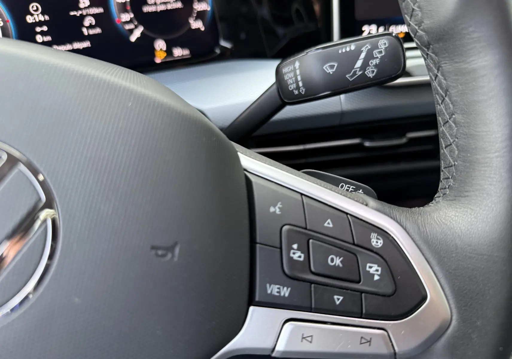 Gros plan sur le volant côté gauche d’une Volkswagen Golf SW gris lunaire, avec commandes multifonctions et tableau de bord numérique.