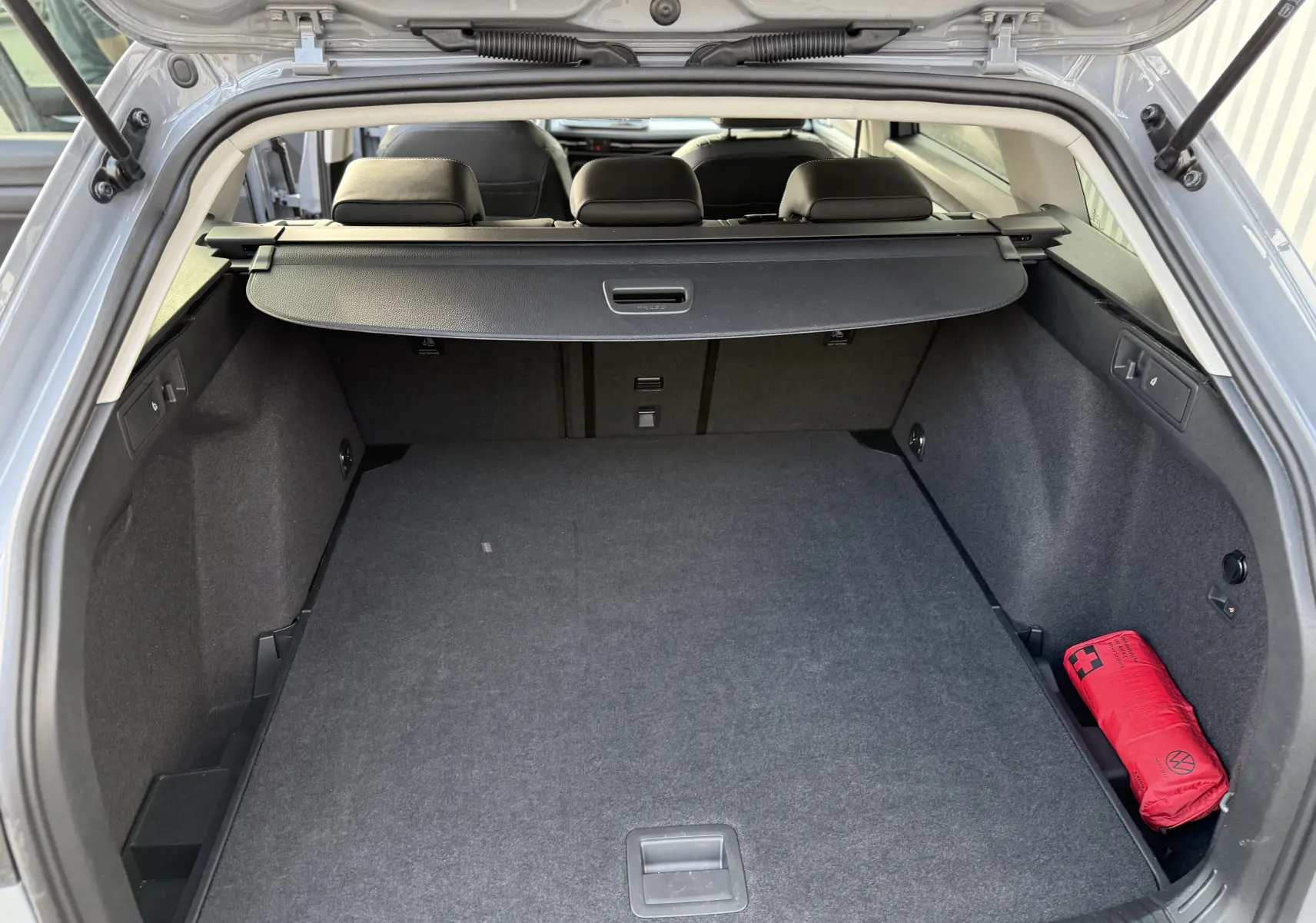 Vue arrière du coffre gris lunaire de la Volkswagen Golf SW 2.0 TDI 150, avec cache-bagages et trousse de secours rouge.