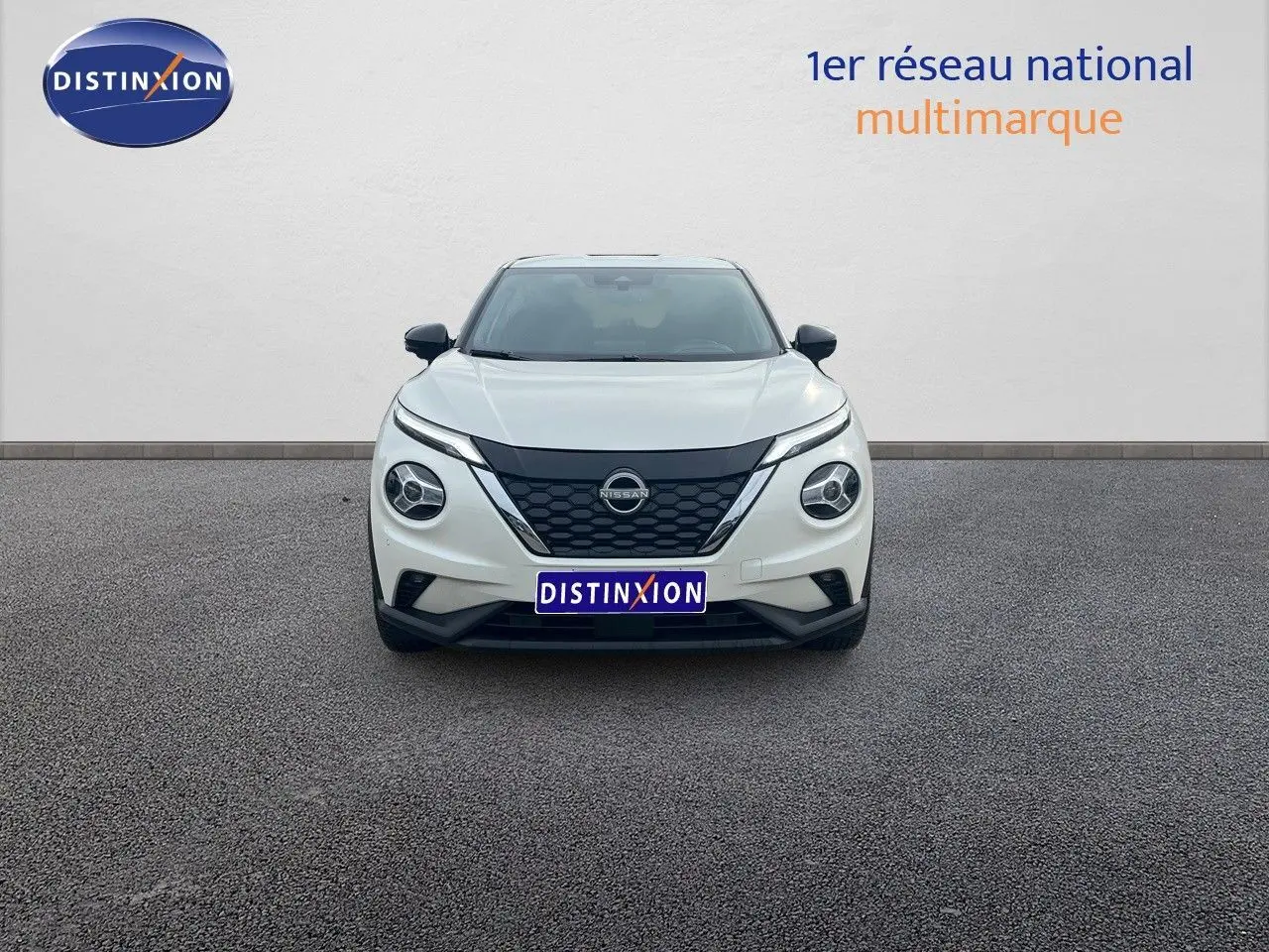 Vue frontale d'un Nissan Juke blanc nacré 2024 avec calandre noire et phares ronds distinctifs.