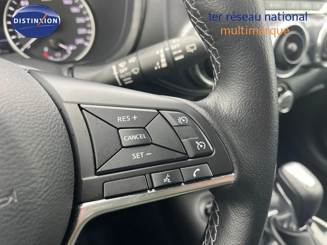 Gros plan sur les commandes de régulateur de vitesse au volant cuir noir du Nissan Juke blanc nacré 2024.