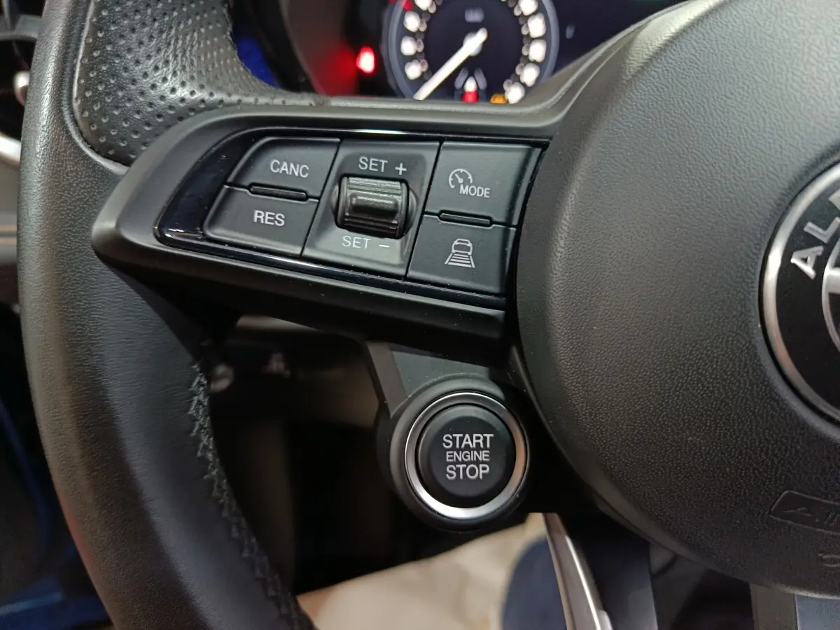 Gros plan sur le volant noir de l'Alfa Romeo Tonale avec les commandes de régulateur et le bouton start engine stop.