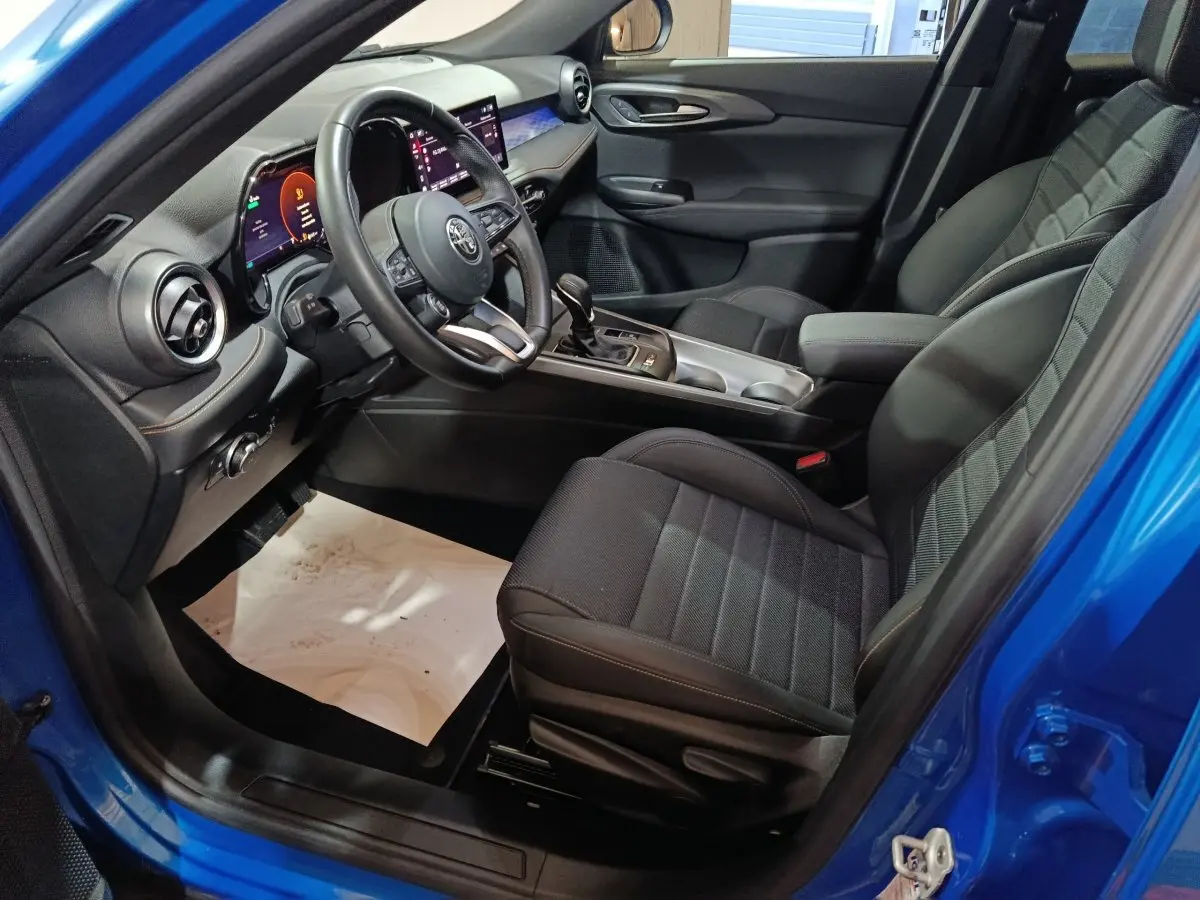 Vue intérieure côté conducteur de l'Alfa Romeo Tonale bleu, montrant sièges noirs et tableau de bord digital moderne.