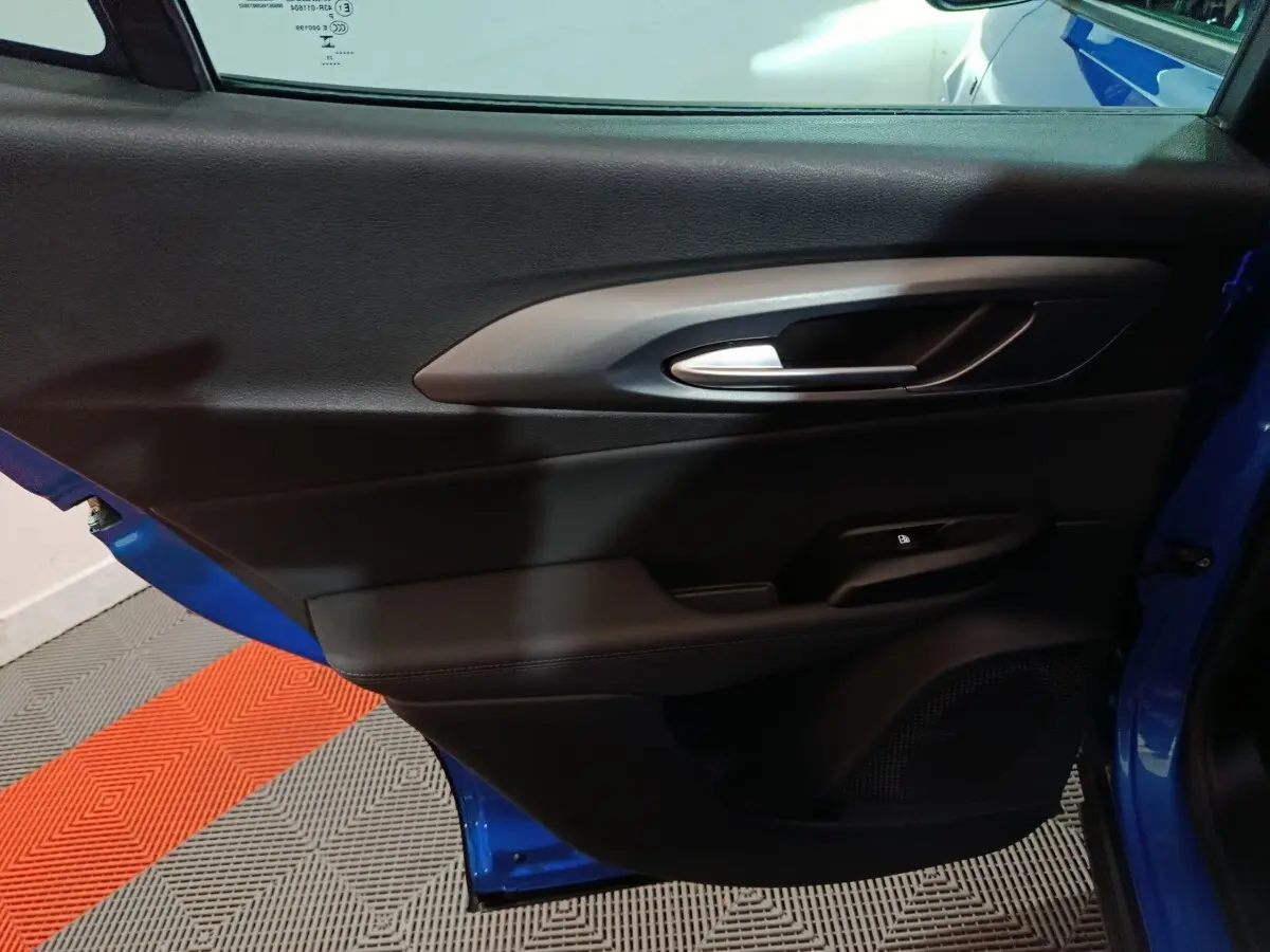 Vue intérieure côté gauche de la porte avant bleu de l'Alfa Romeo Tonale avec poignée argentée et commande de verrouillage.