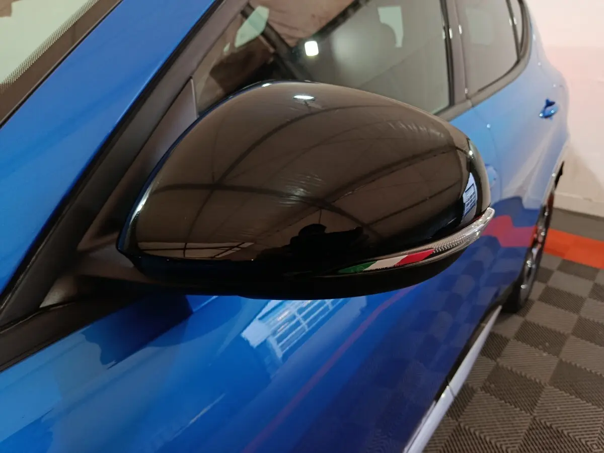 Gros plan sur le rétroviseur noir côté conducteur d'une Alfa Romeo Tonale bleu 2023 avec drapeau italien intégré.