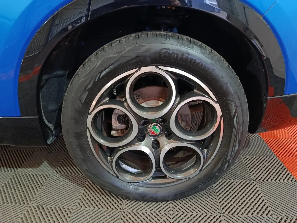 Gros plan sur la roue avant droite bleue d'une Alfa Romeo Tonale 1.3T PHEV avec jante distinctive à cinq cercles.