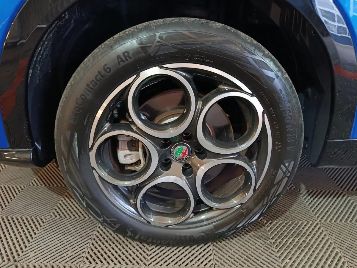 Gros plan sur la roue avant droite bleue d'une Alfa Romeo Tonale avec jante en alliage à cinq cercles distinctifs.