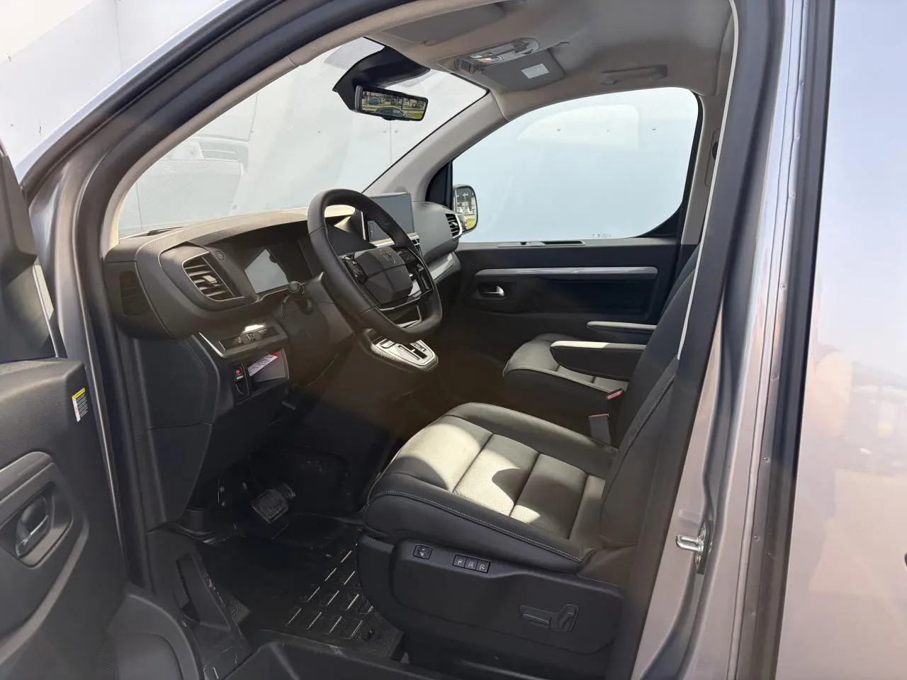 Vue intérieure côté conducteur du Citroën Jumpy gris acier, montrant sièges cuir et tableau de bord moderne.