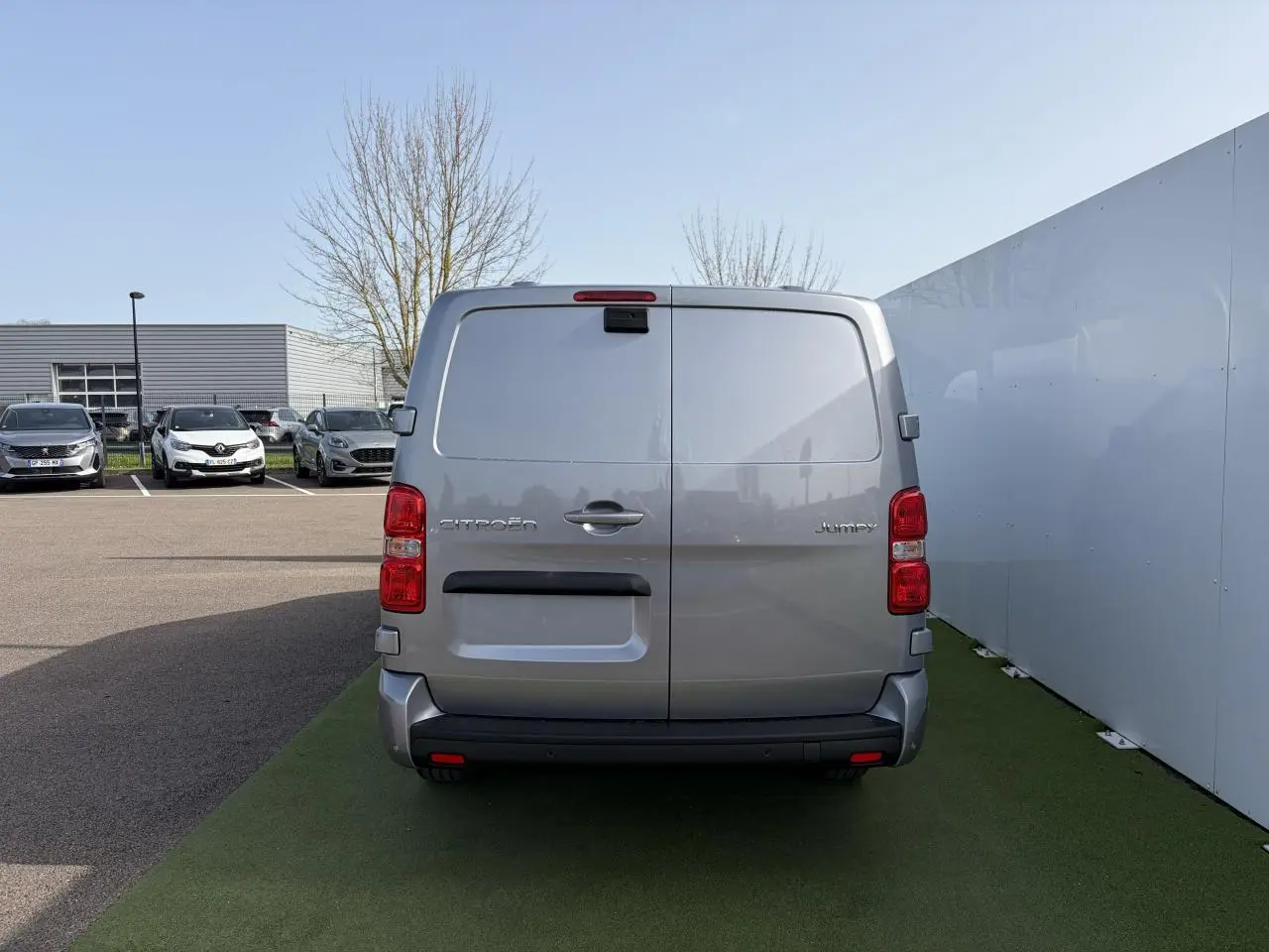 Vue arrière d'un Citroën Jumpy gris acier métal stationné, avec portes battantes et feux rouges verticaux.