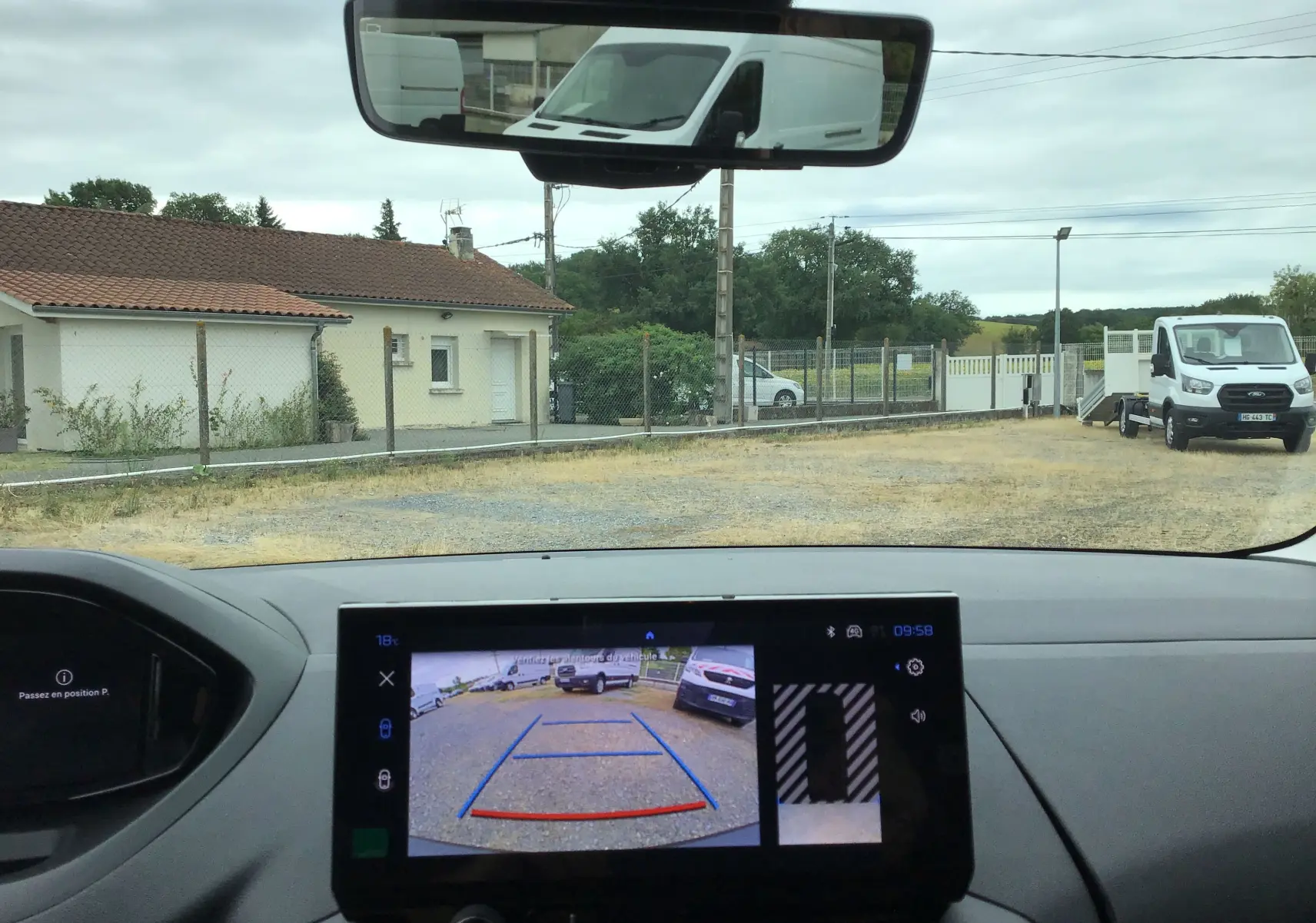 Vue intérieure du tableau de bord du Peugeot Partner blanc 2026, avec écran de caméra de recul et rétroviseur central visible.