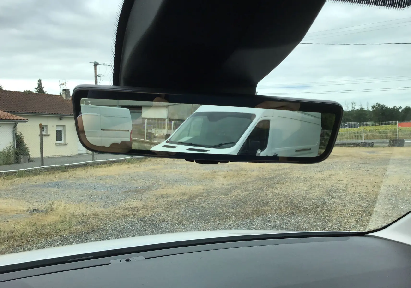Rétroviseur intérieur montrant un Peugeot Partner blanc en vue arrière sur un terrain extérieur.