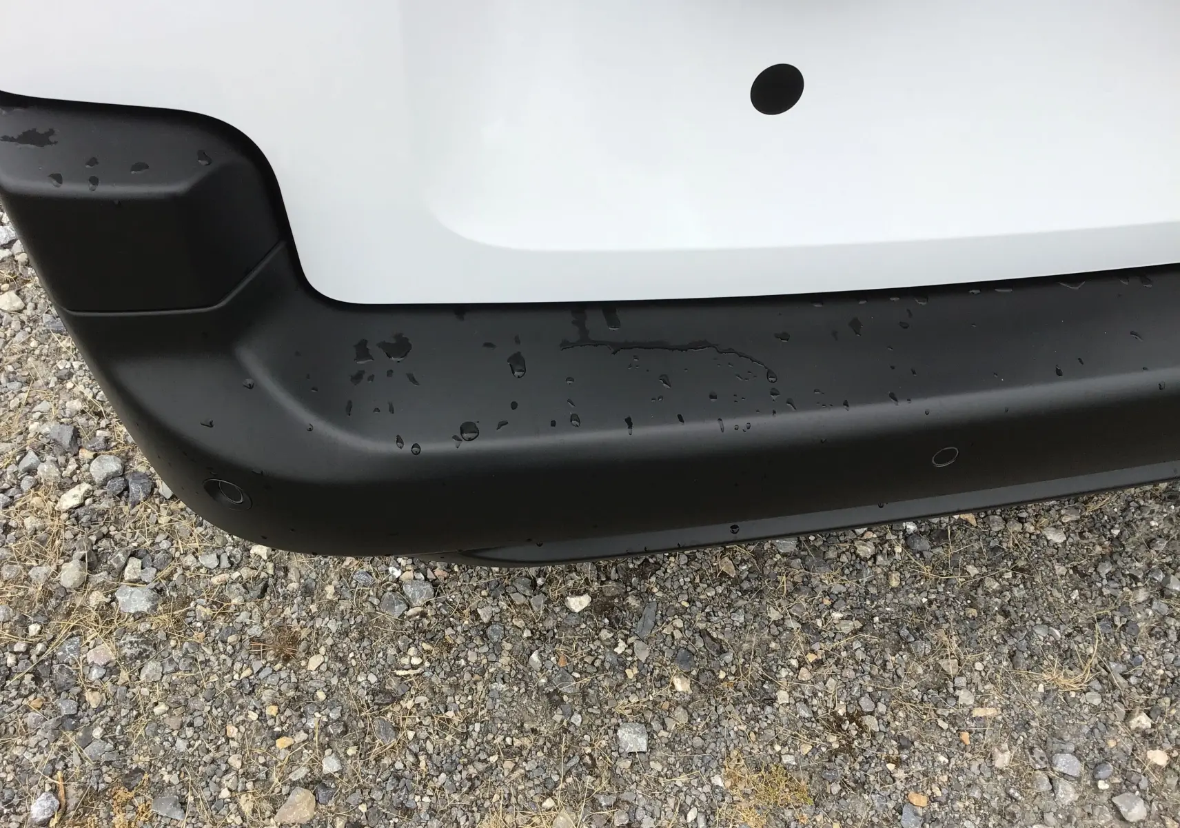 Gros plan sur le pare-chocs arrière noir du Peugeot Partner XL blanc, avec capteurs de recul visibles et traces d'eau.