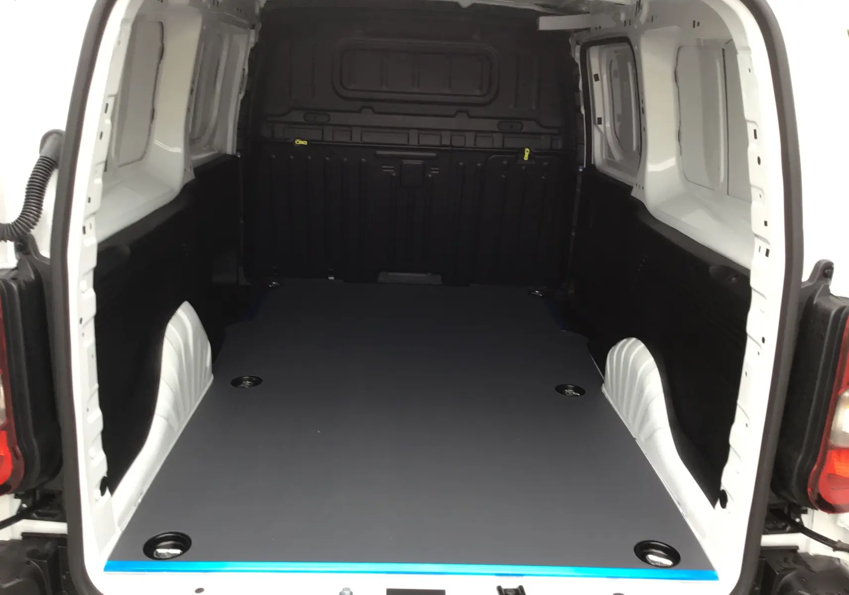 Vue arrière du Peugeot Partner blanc montrant l’espace de chargement avec plancher antidérapant et parois noires.