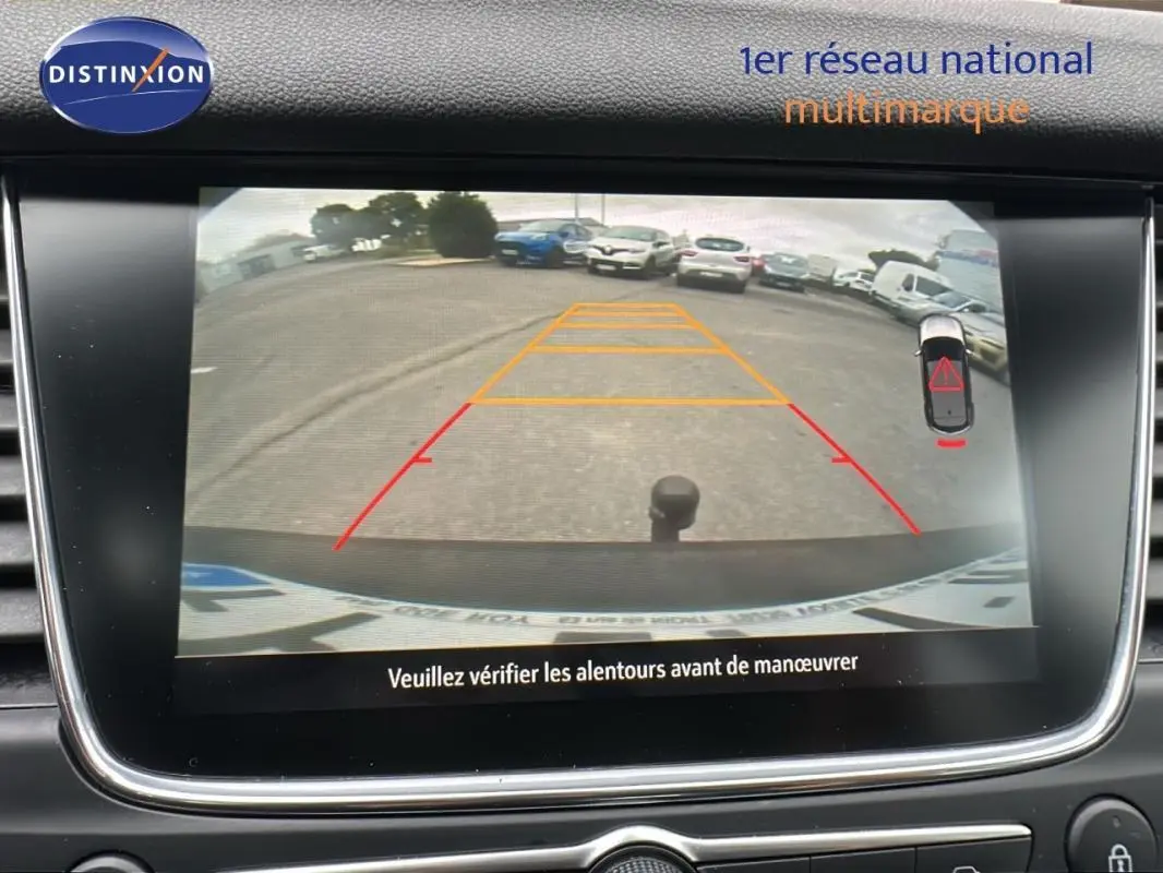 Écran tactile intérieur montrant la caméra de recul d'un Opel Grandland X gris clair avec attelage visible.