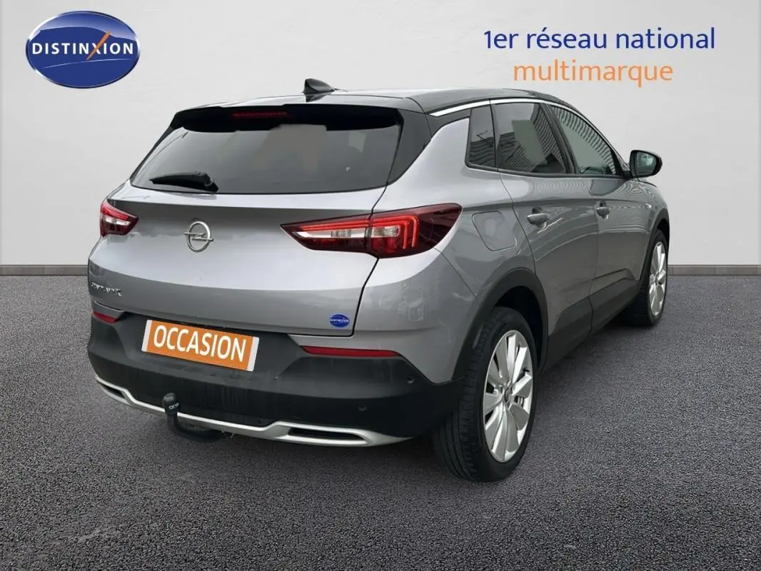 Opel Grandland X gris clair vu en 3/4 arrière droit, avec attelage et jantes alliage 19 pouces visibles.