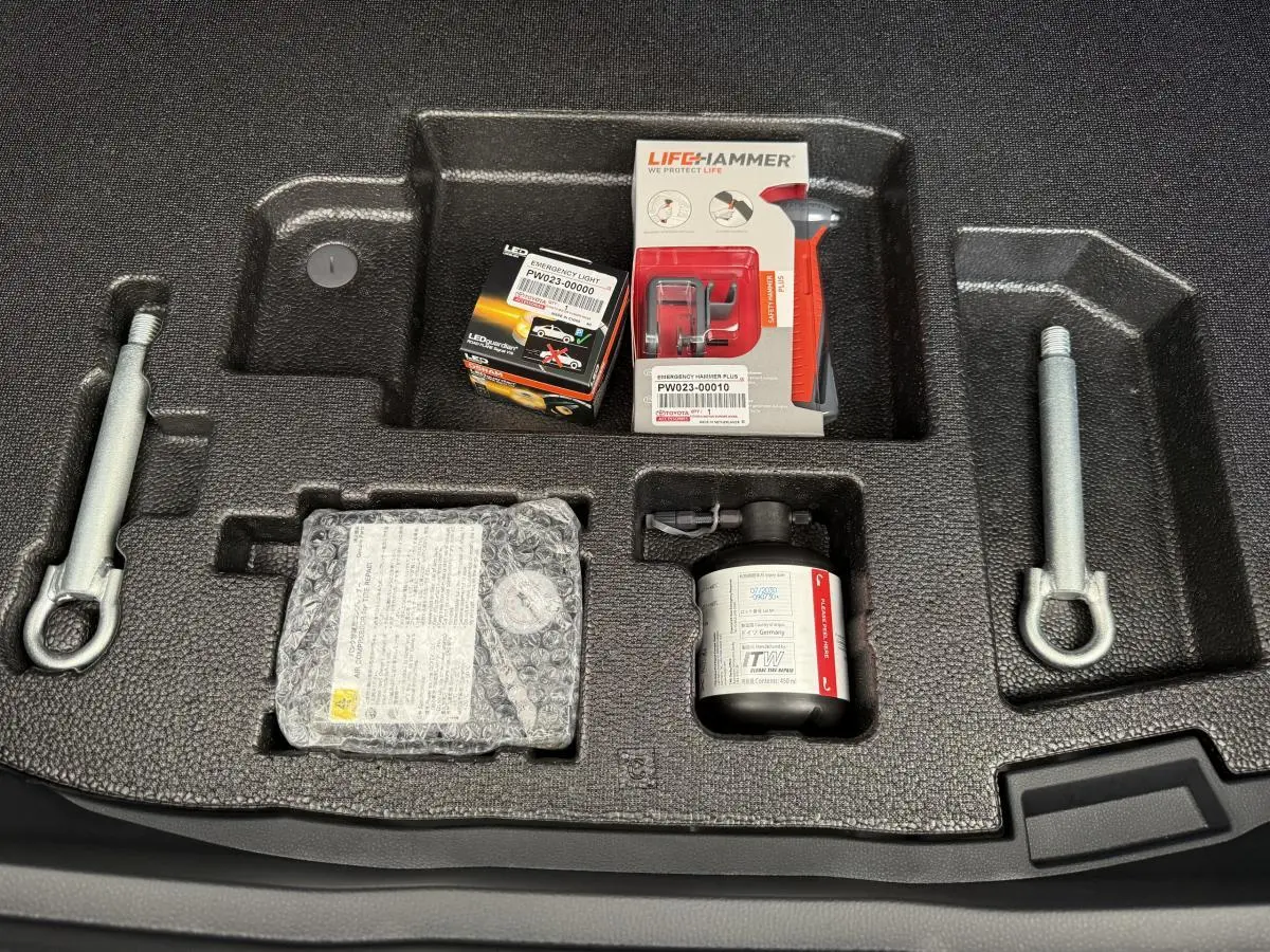 Vue plongeante sur le coffre du Toyota C-HR blanc 2024 montrant le kit anticrevaison et outils de secours.