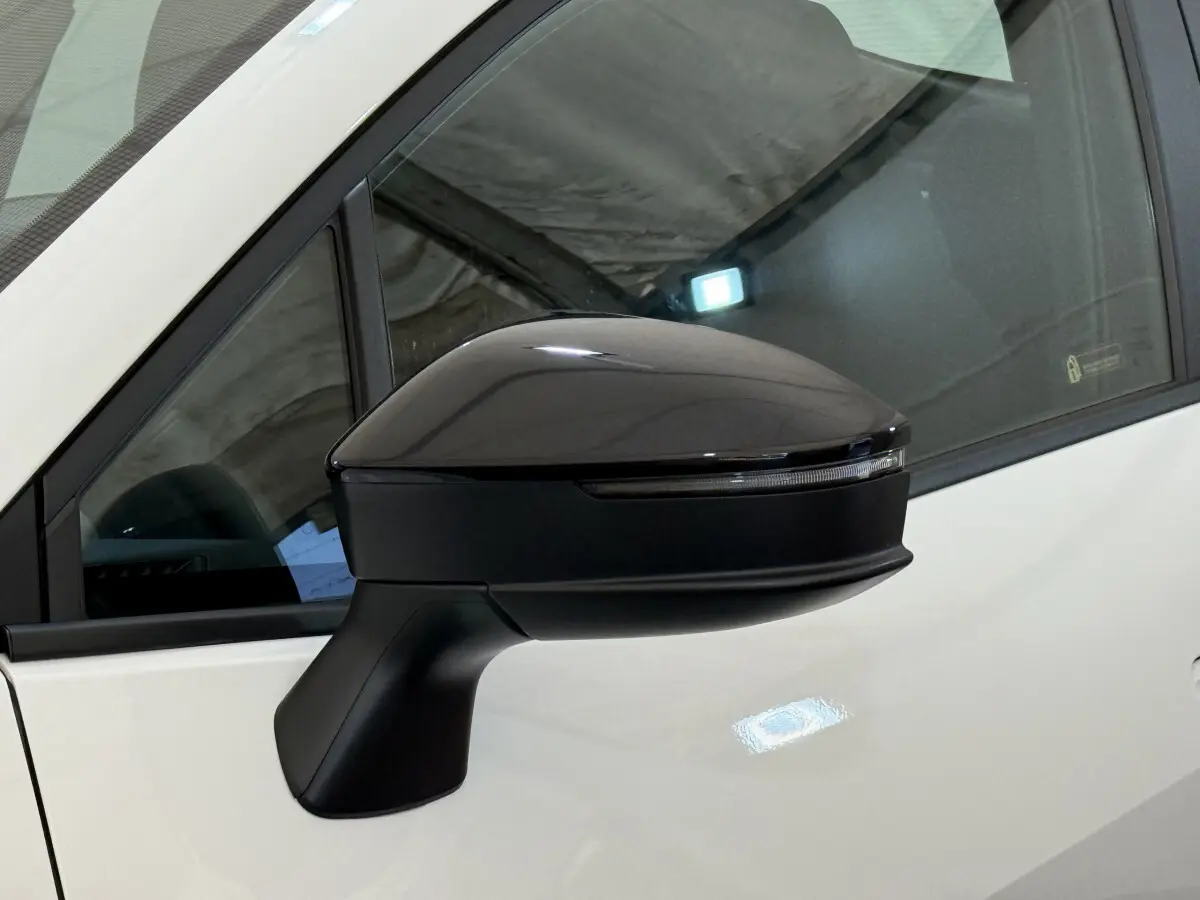 Rétroviseur côté gauche noir brillant du Toyota C-HR blanc 2024, avec clignotant intégré visible en gros plan.