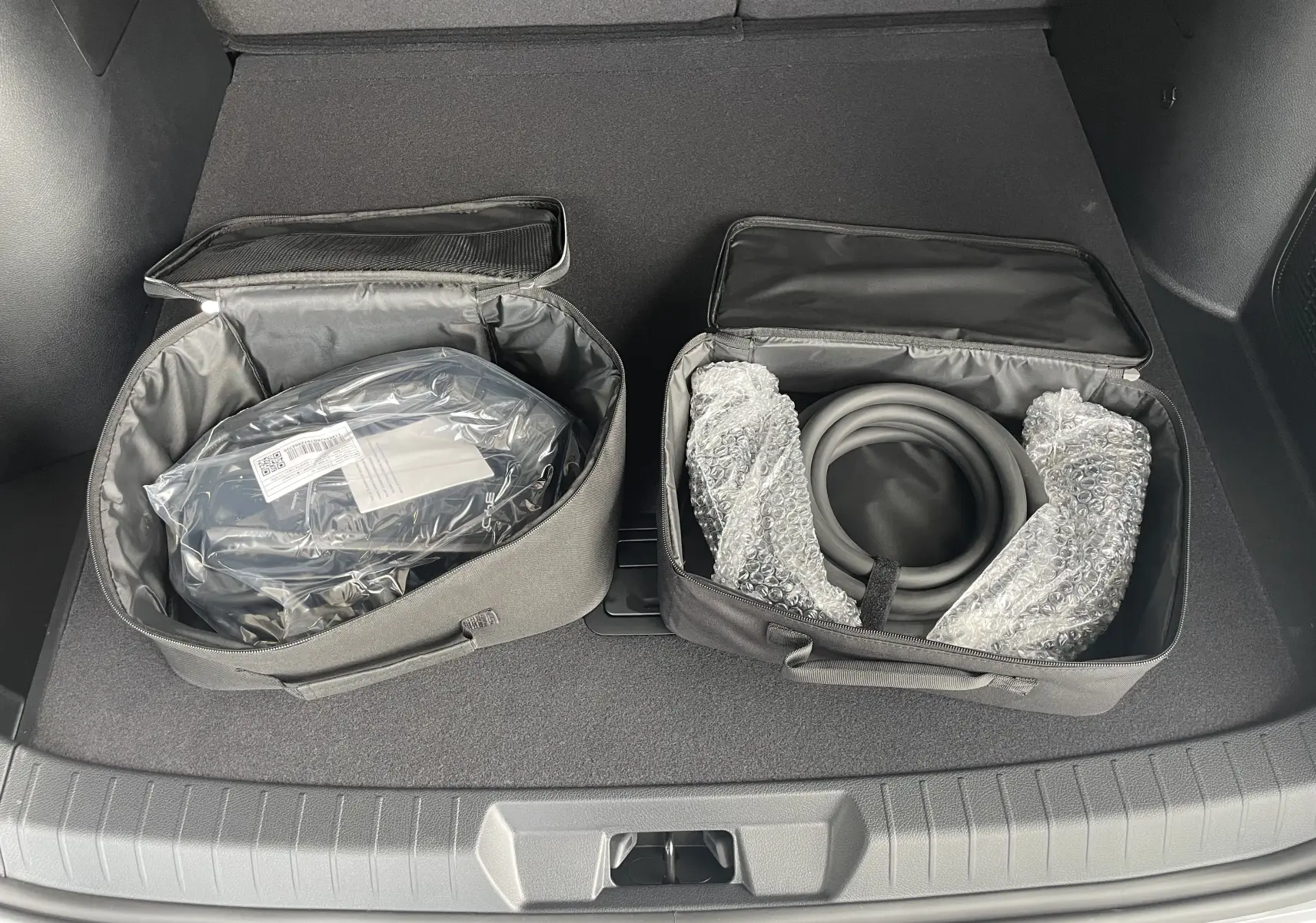 Vue du coffre du BYD SEAL U 2025 avec deux sacs de rangement noirs contenant câbles de recharge, intérieur gris foncé.