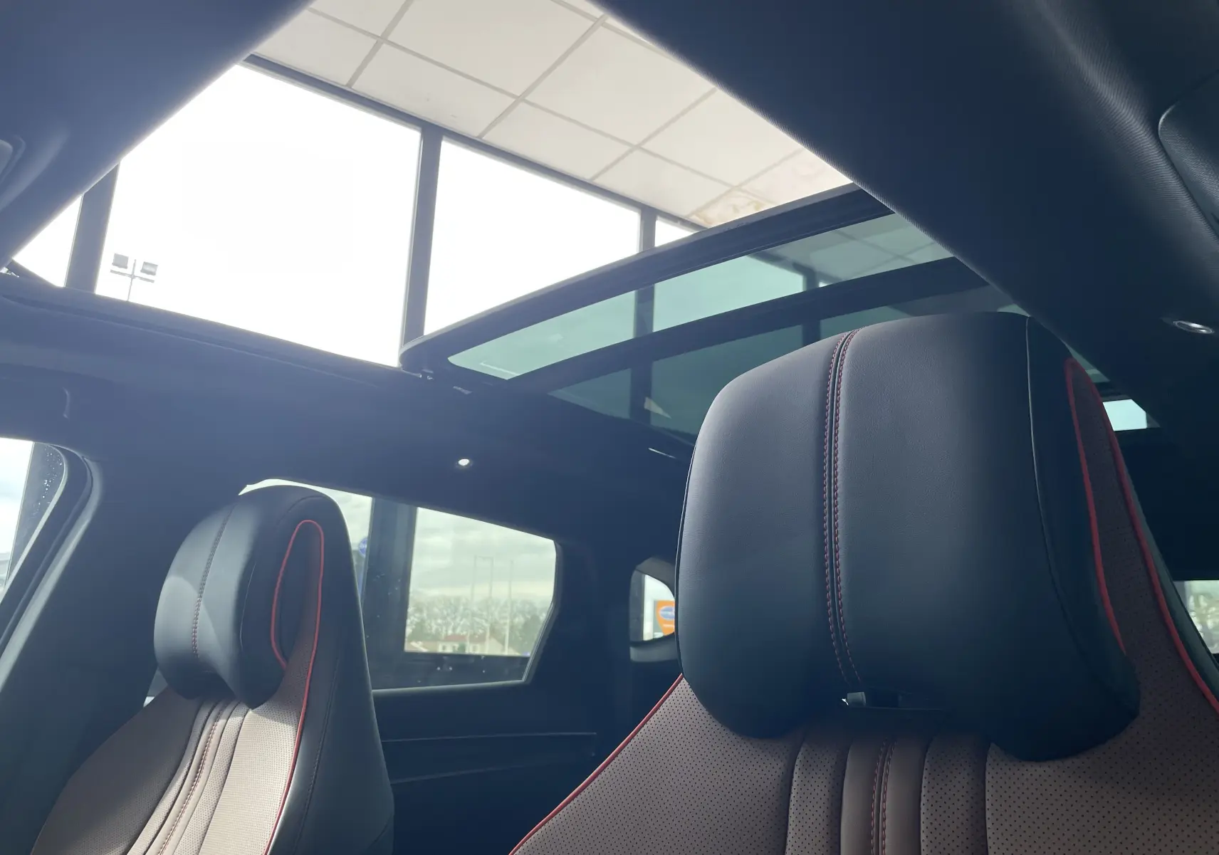 Intérieur du BYD SEAL U 2025 avec toit ouvrant panoramique et sièges en similicuir noir à surpiqûres rouges.