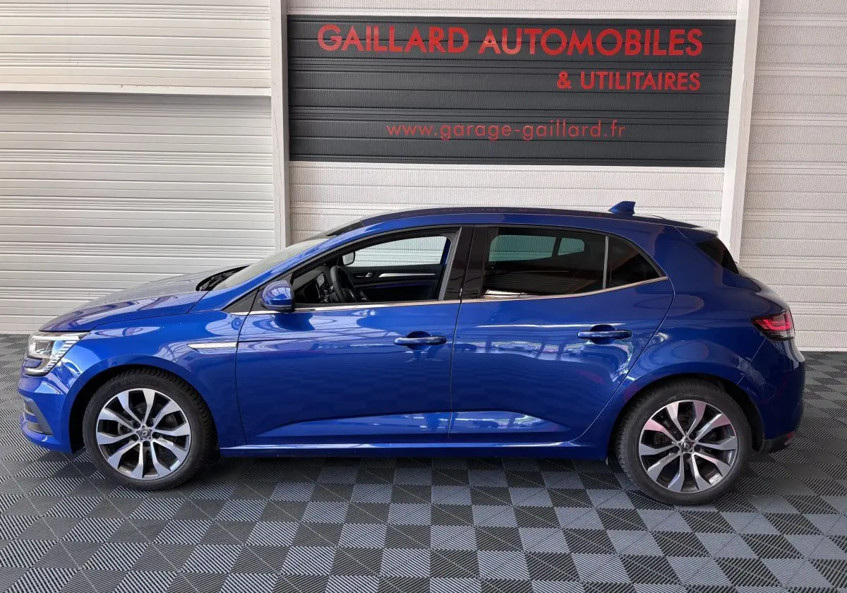 Profil côté gauche de la Renault Mégane bleu 2023 avec jantes alliage et vitres teintées, en intérieur showroom.