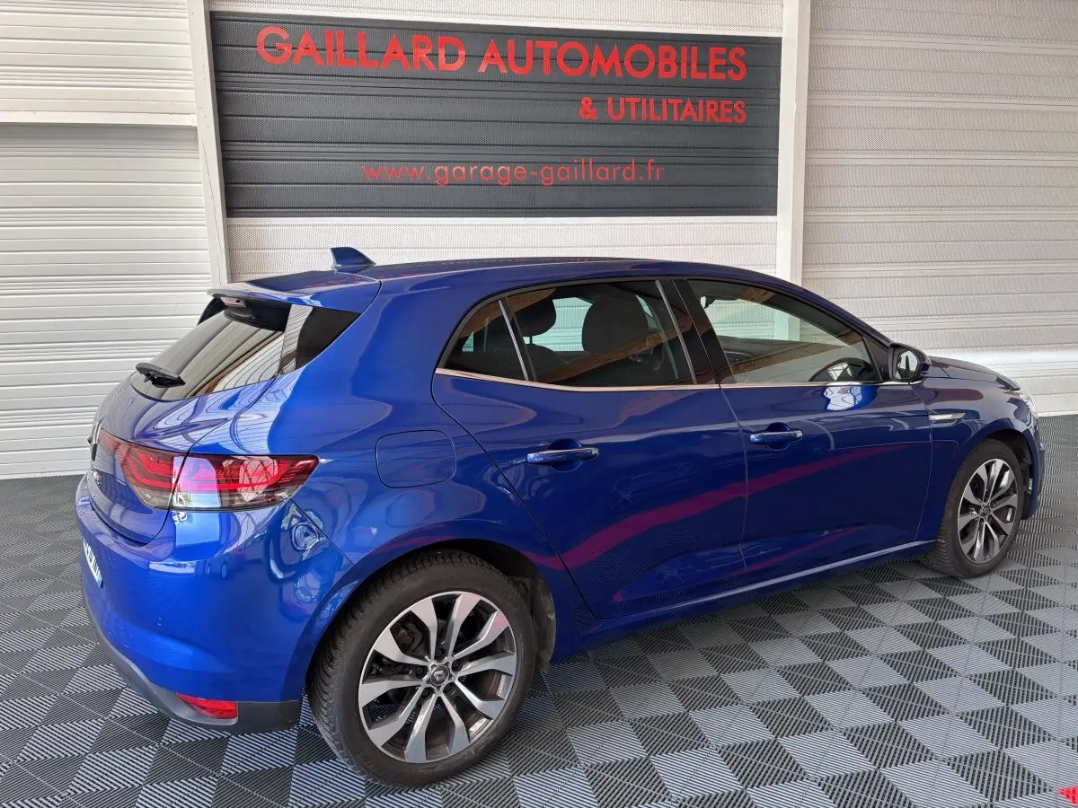 Renault Mégane bleu vue 3/4 arrière côté droit, avec vitres teintées et jantes alliage, en intérieur garage.
