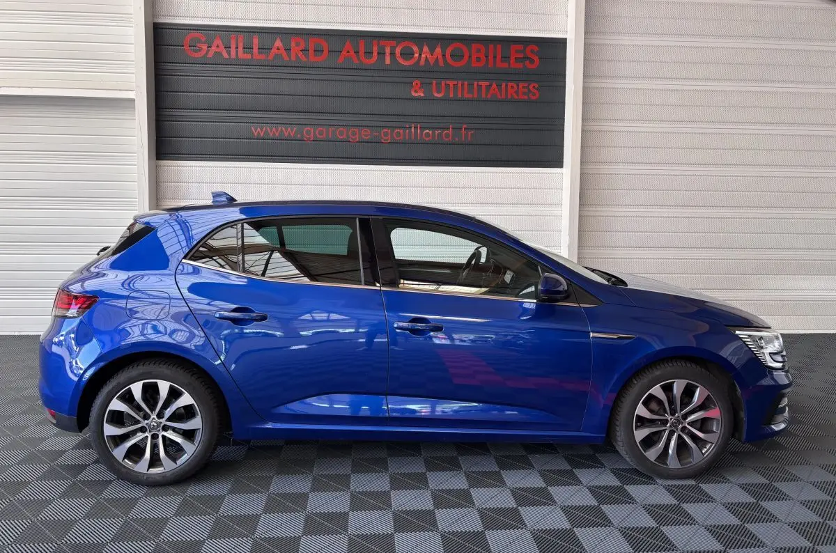 Profil côté gauche d'une Renault Mégane bleu 2023 garée en intérieur avec jantes alliage distinctives.