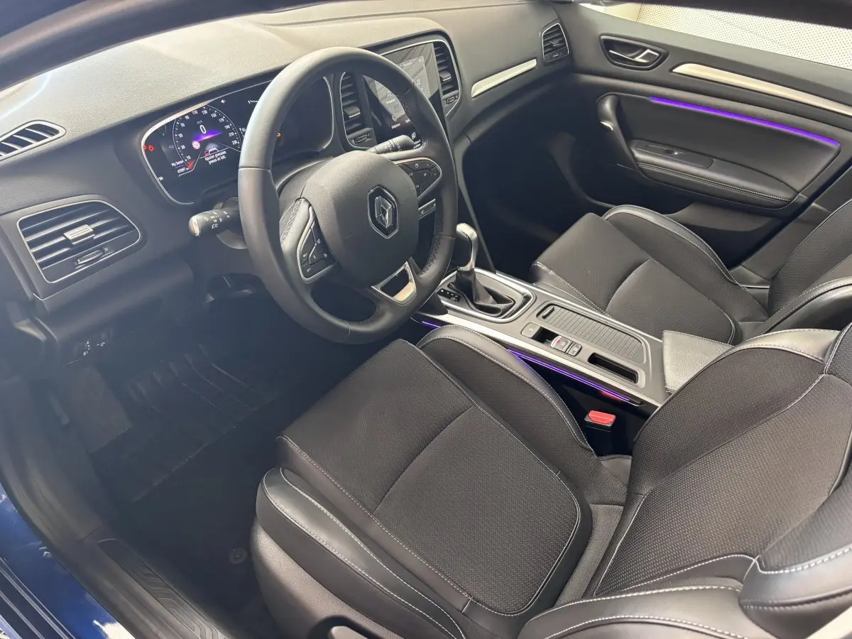 Intérieur de la Renault Mégane 2023 vue côté conducteur, volant multifonctions et éclairage d'ambiance violet visible.