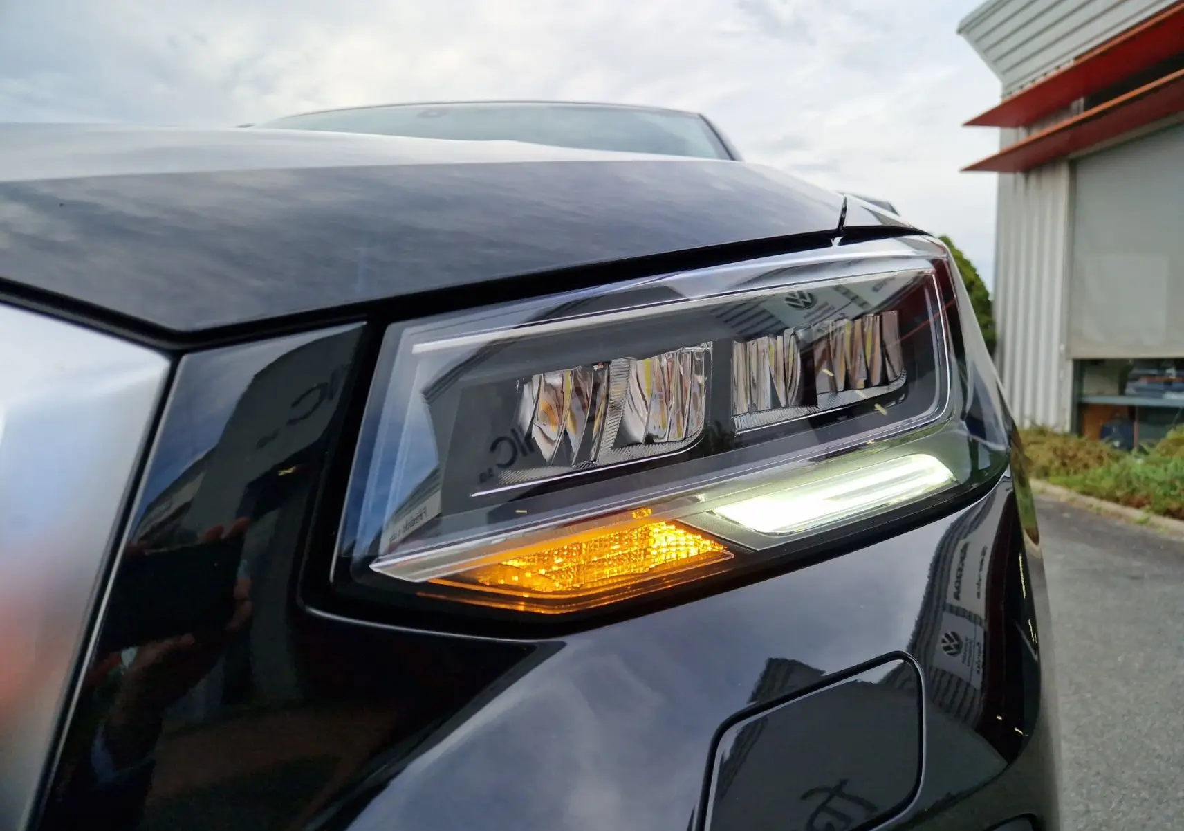 Gros plan sur le phare avant droit d'un Audi Q2 2023 noir mito metal avec clignotant allumé et LED diurne.