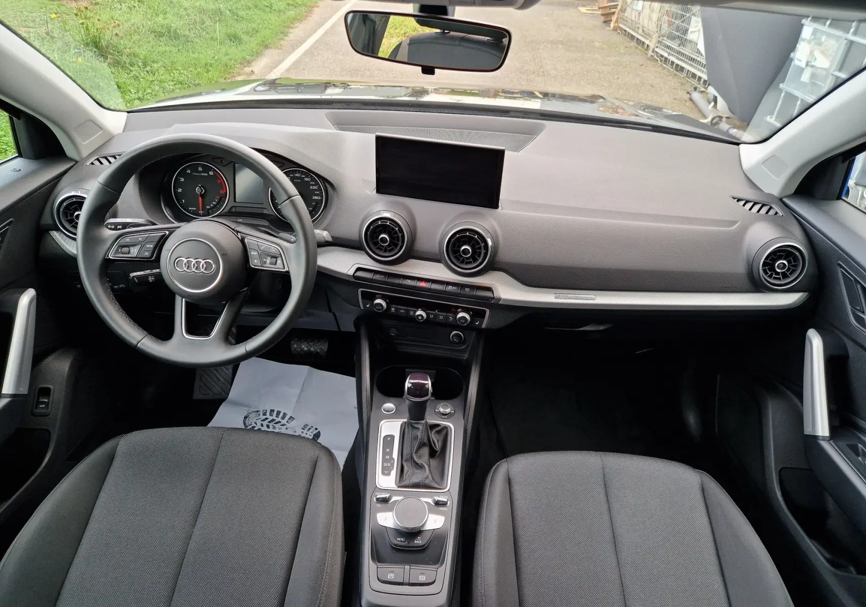 Vue intérieure de l'Audi Q2 35 TFSI 2023 montrant le tableau de bord gris clair, volant multifonction et sièges tissu noir.