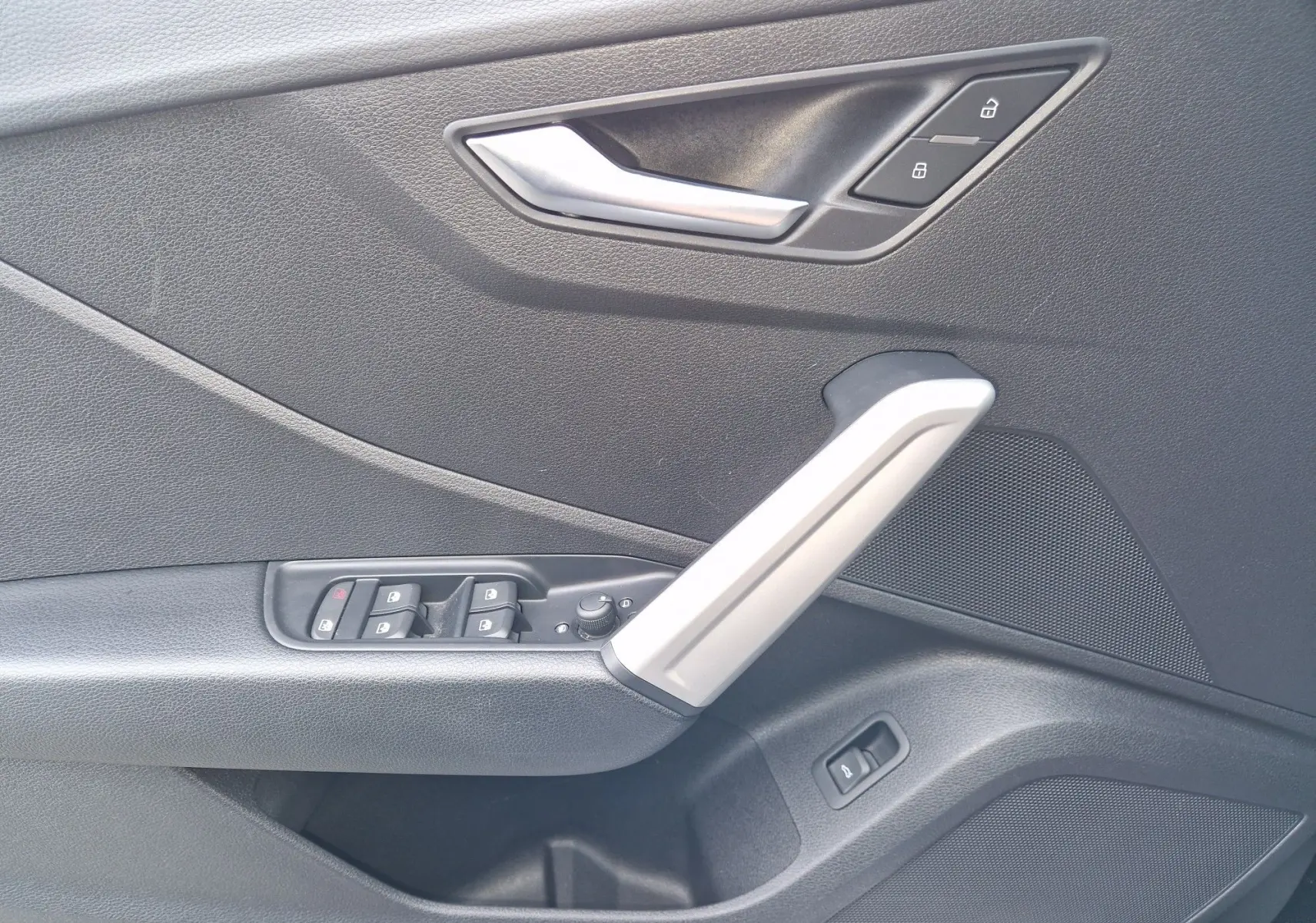 Détail de la porte côté gauche de l'Audi Q2 2023 noir mito metal avec commandes de vitres et poignée argentée.
