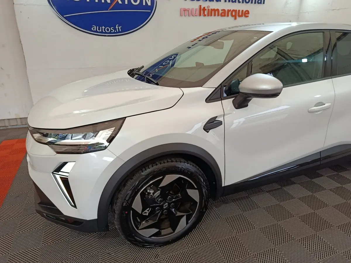 Vue de profil avant droit d'un Renault Captur blanc avec jantes noires et détails modernes sur l'aile avant.
