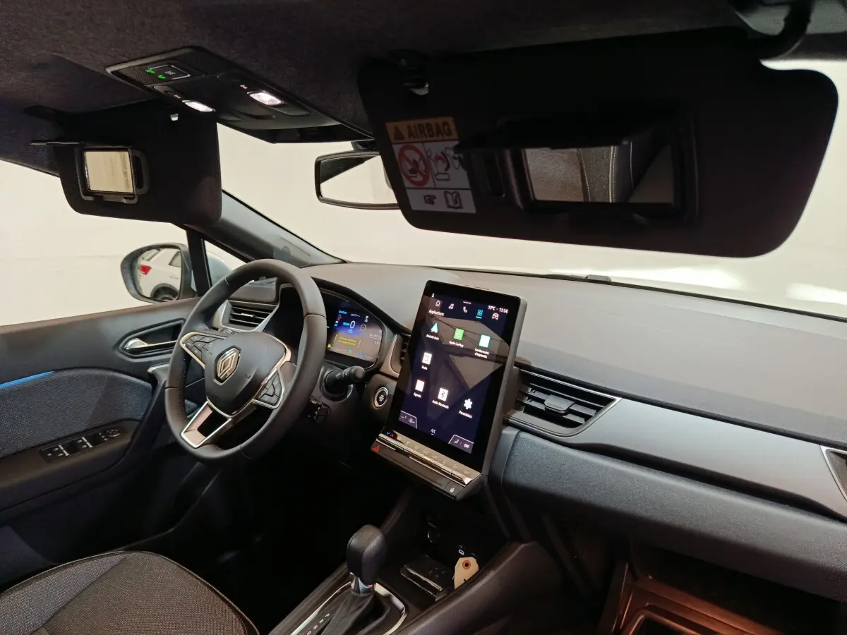 Intérieur du Renault Captur blanc 2025, vue côté conducteur, tableau de bord avec écran tactile vertical et volant multifonctions.