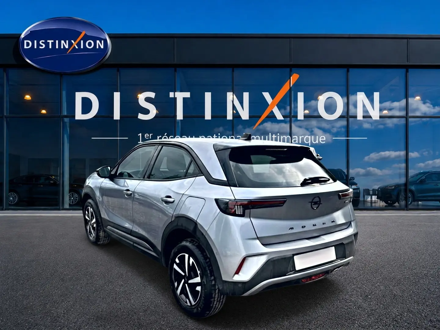 Vue 3/4 arrière droite d'un Opel Mokka gris 2025 devant une vitrine Distinxion, avec feux arrière LED et jantes noires.