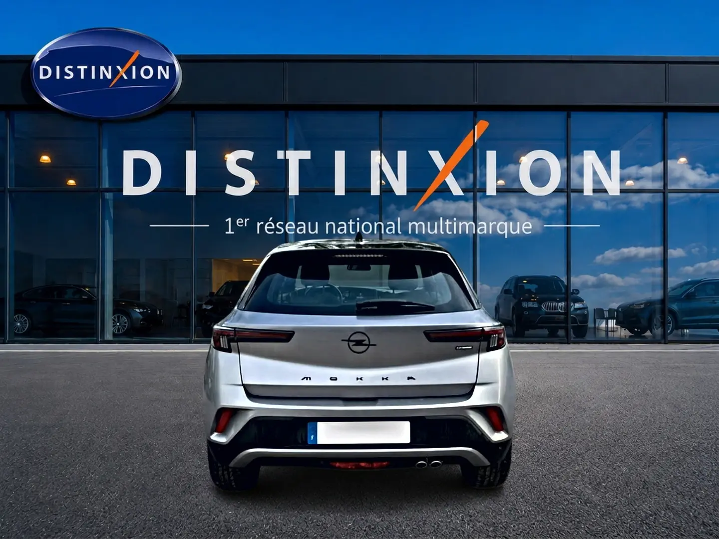 Vue arrière d'un Opel Mokka gris 2025 garé devant une vitrine avec logo Distinxion en arrière-plan.