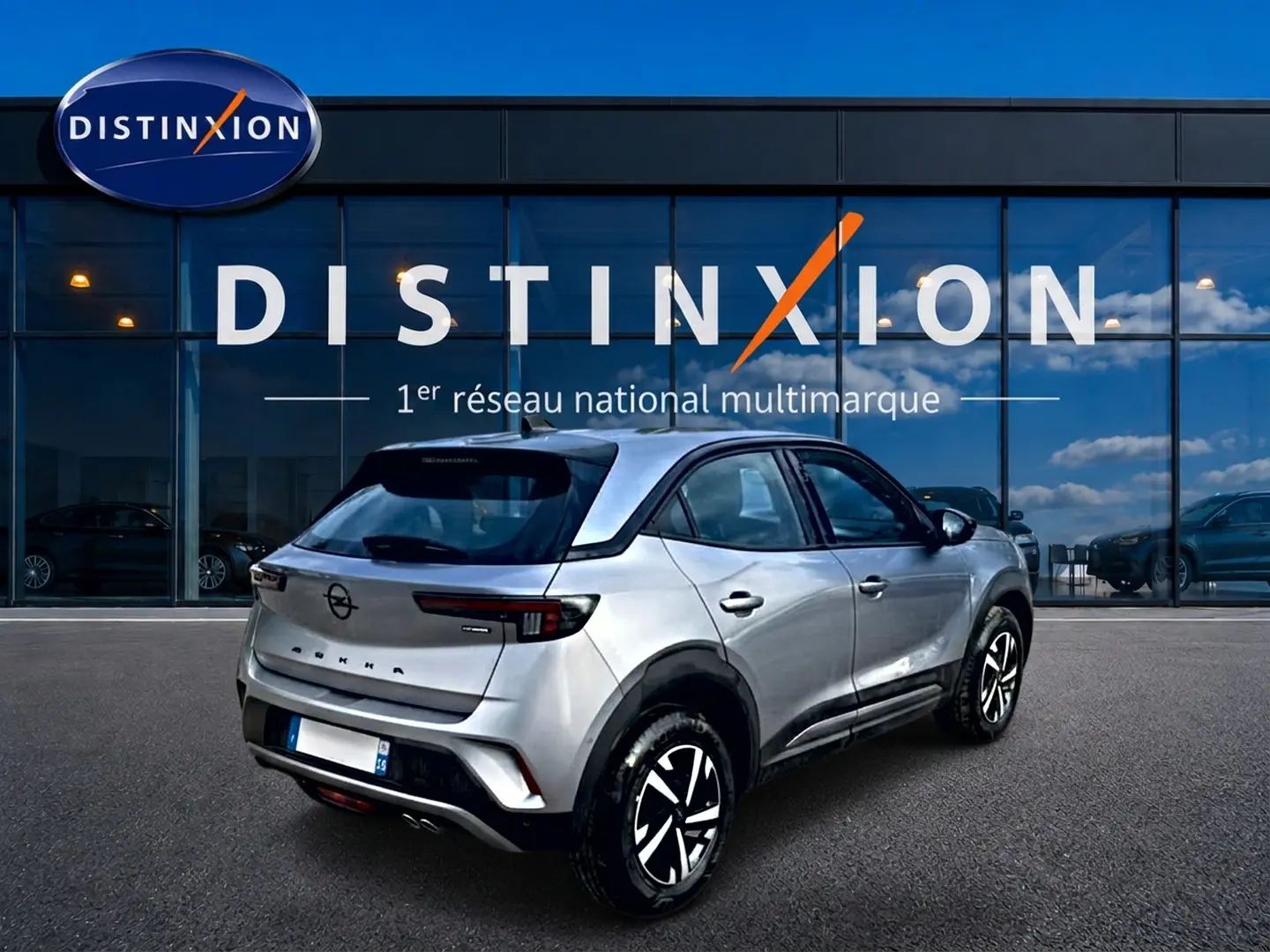 Vue 3/4 arrière droite d'un Opel Mokka gris 2025 devant une vitrine Distinxion, avec feux arrière LED et jantes stylisées.