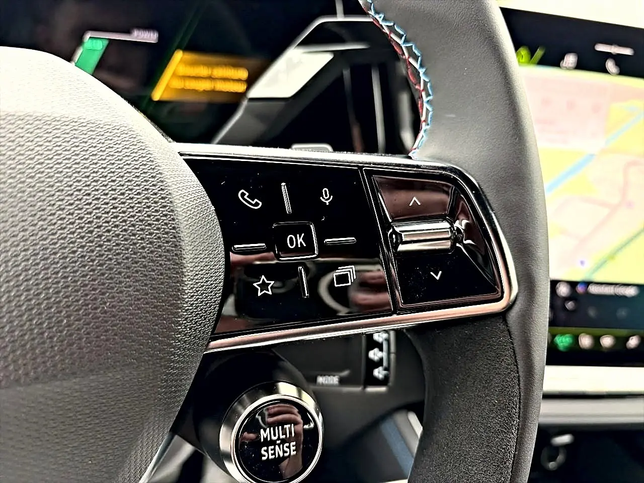 Gros plan sur le volant noir avec commandes multifonctions et molette Multi-Sense du Renault Austral gris schiste, tableau de bord en arrière-plan.