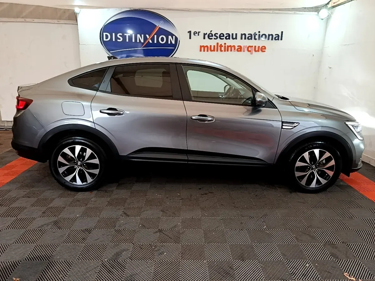 Profil côté gauche d'une Renault Arkana Business E-TECH 145 gris foncé dans un showroom avec logo Distinxion en arrière-plan