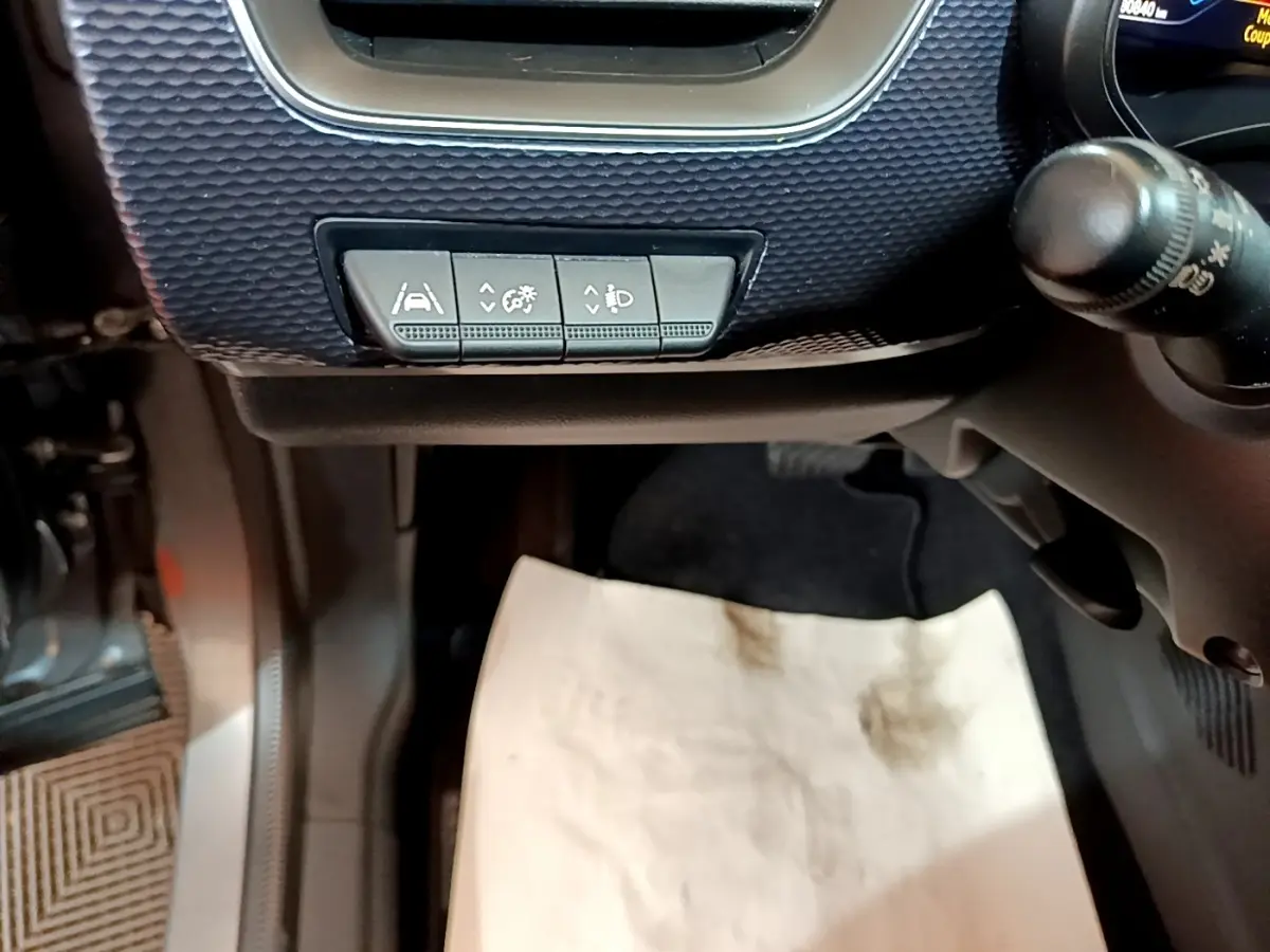 Gros plan sur les commandes sous le tableau de bord côté gauche d’un Renault Arkana gris foncé, avec pédalier et tapis de sol visible.