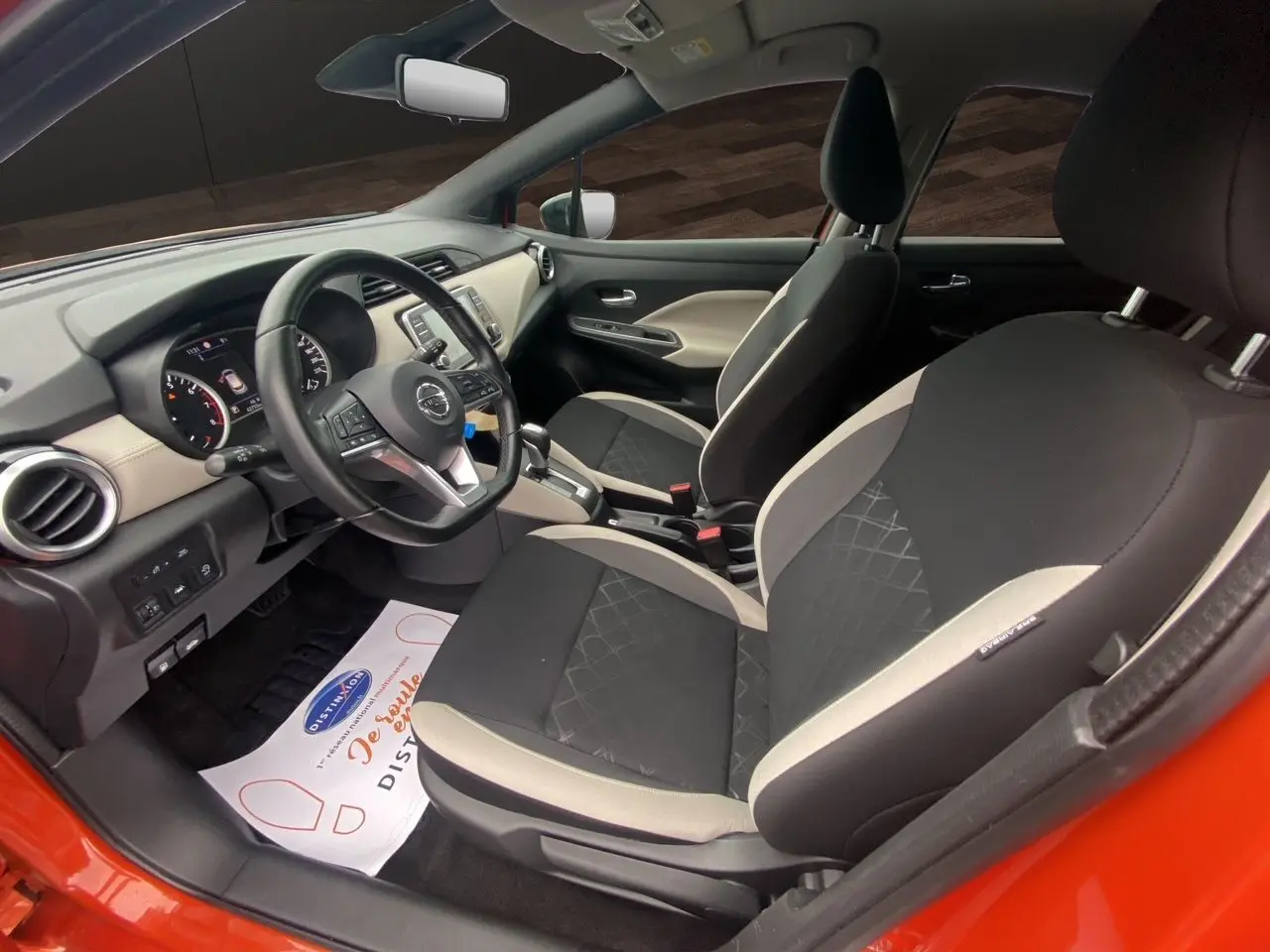 Vue intérieure côté conducteur de la Nissan Micra orange energy 2022, sièges tissu noir et beige avec volant multifonction.