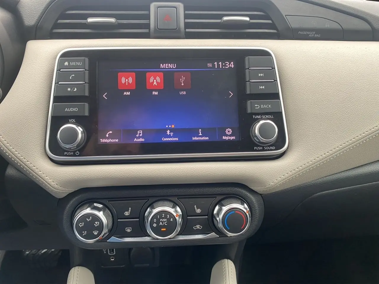 Vue rapprochée de la console centrale beige et noire de la Nissan Micra 2022 avec écran tactile et commandes de climatisation.