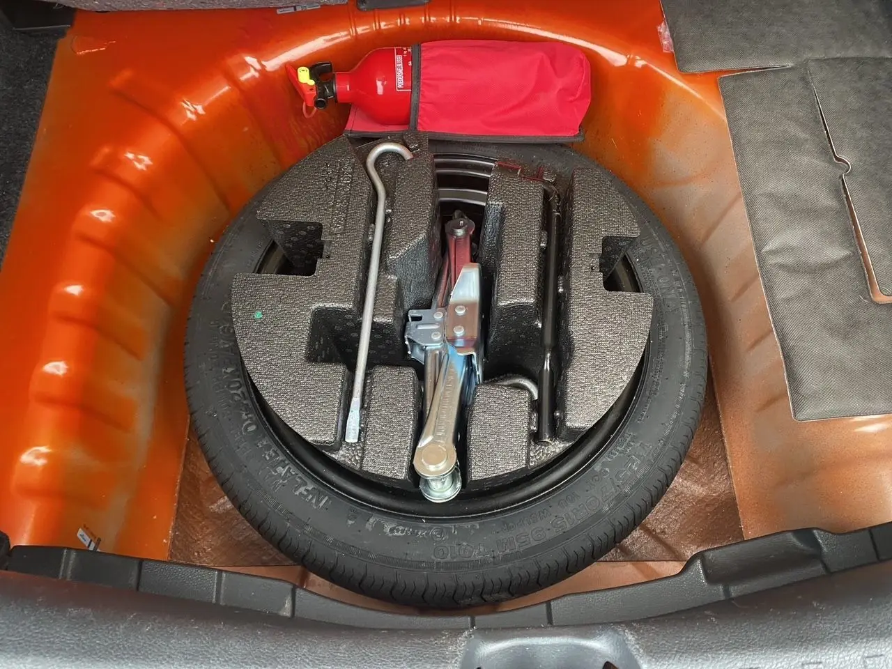 Vue plongeante sur la roue de secours et les outils dans le coffre orange energy d'une Nissan Micra 2022.