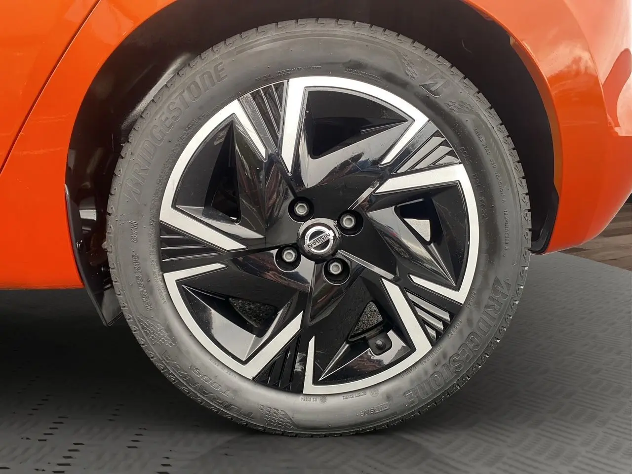 Gros plan sur la roue avant droite d’une Nissan Micra orange Energy, jante alliage noir et argent au design géométrique.