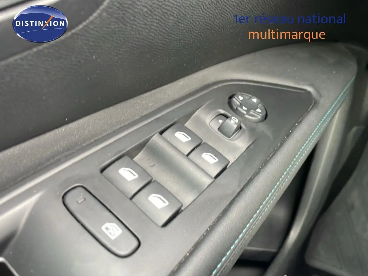 Gros plan sur les commandes de lève-vitres et rétroviseurs côté conducteur avec surpiqûres bleues sur la porte intérieure.