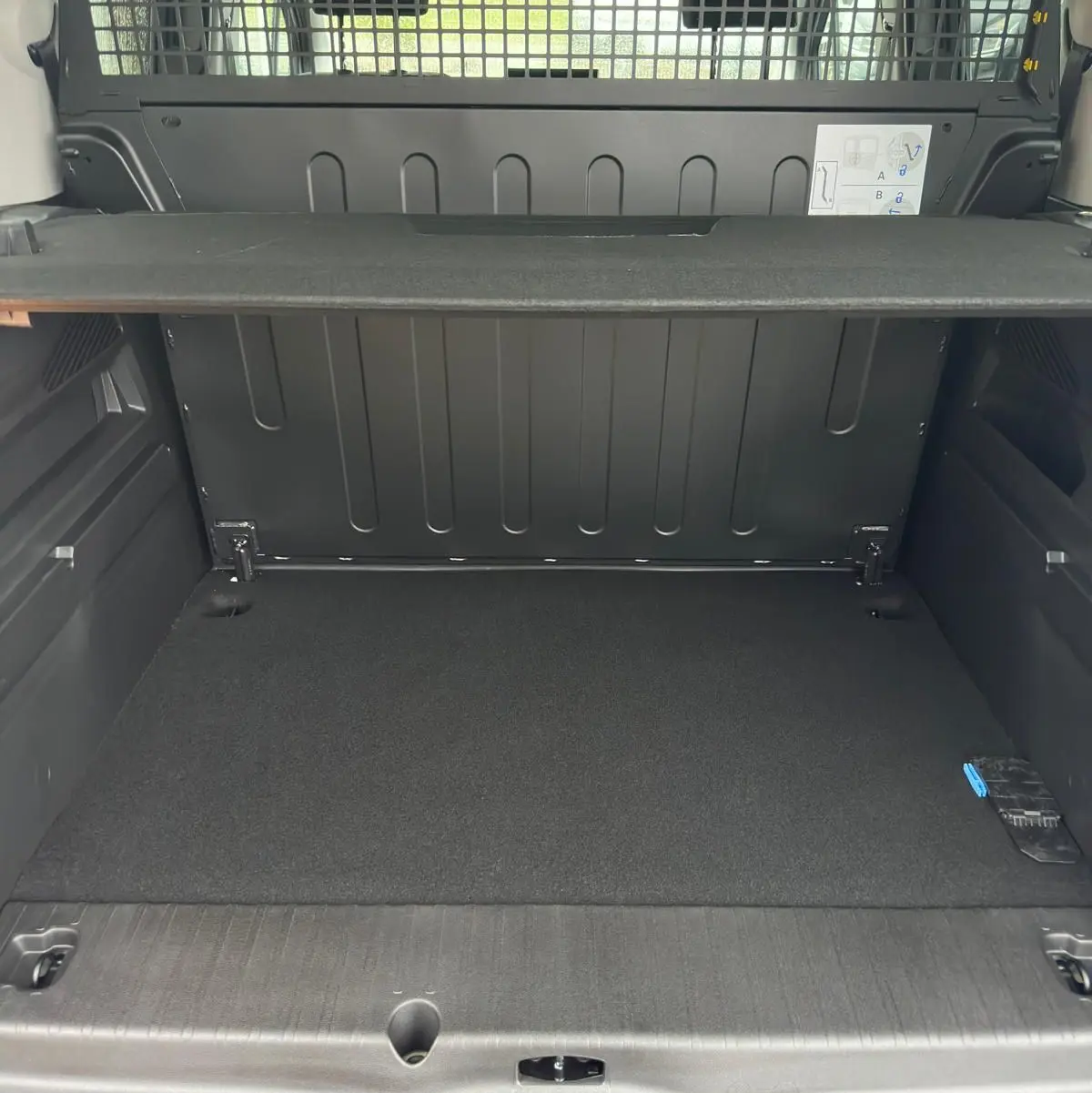 Vue intérieure arrière du coffre gris du Citroën Berlingo N1 2025 avec séparation grillagée et tablette de rangement.