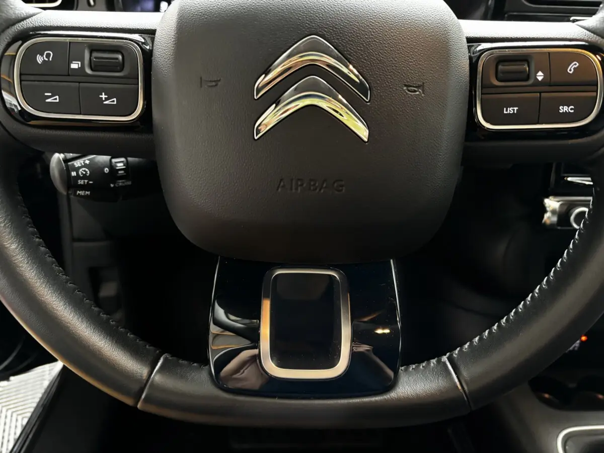 Gros plan sur le volant noir multifonctions de la Citroën C3 2024 avec commandes intégrées et logo chromé central.