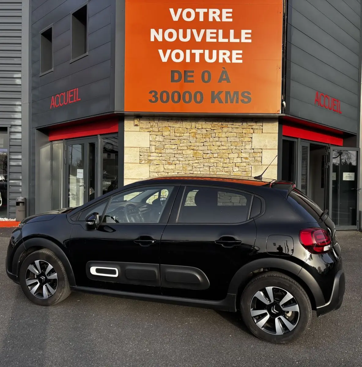 Profil droit d'une Citroën C3 PureTech 110 Shine noire, avec protections latérales et jantes distinctives, devant un bâtiment.
