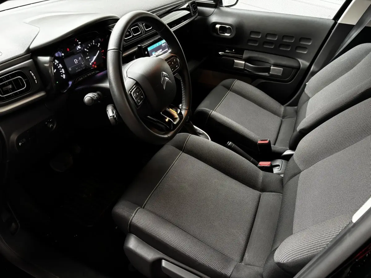 Vue intérieure de la Citroën C3 PureTech 110 2024, côté conducteur, avec volant multifonctions et sièges tissu gris.