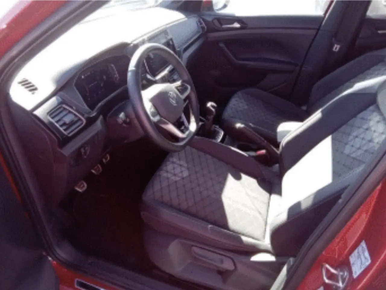 Vue intérieure côté conducteur du Volkswagen T-Cross rouge métal 2025, avec sièges en tissu et boîte manuelle.
