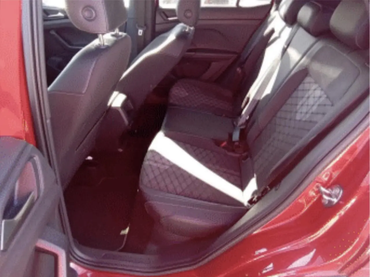 Vue intérieure côté arrière droit du Volkswagen T-Cross rouge métal 2025, sièges arrière en tissu noir à motif losange.